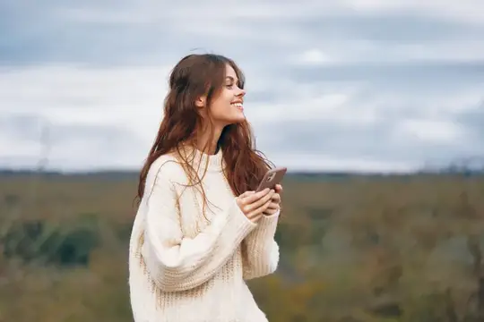 Улыбающаяся девушка с телефоном в руках на фоне осеннего поля