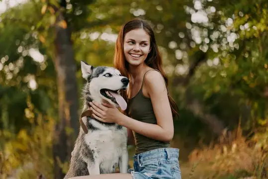 Улыбающаяся девушка обнимает хаски в летнем лесу