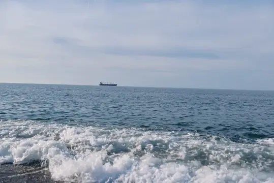 Одинокий грузовой корабль на горизонте спокойного моря