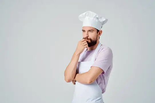 Задумчивый бородатый повар в колпаке и фартуке