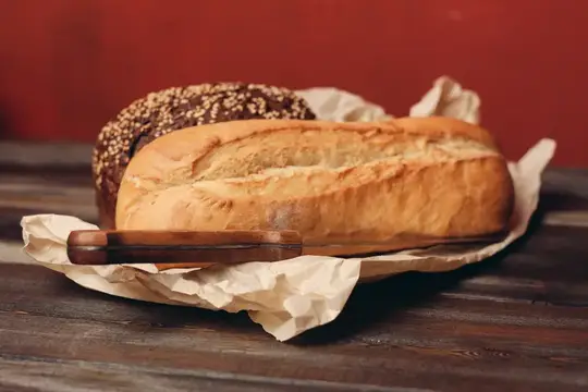 Мука, хлебобулочные изделия, буханка хлеба в бумажной упаковке, острый нож и деревянный стол