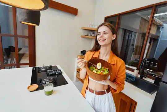 Улыбающаяся девушка с салатом в миске на светлой кухне