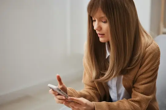 Светловолосая женщина смотрит в смартфон в светлой комнате