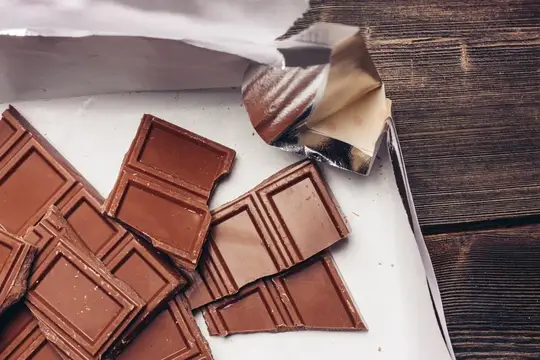 Кусочки молочного шоколада в развёрнутой фольге на деревянном столе
