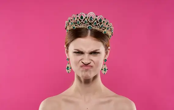Эмоциональная женщина на розовом фоне, сморщенное лицо и диадема, крупный план портрета