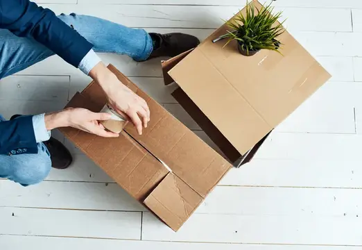 Мужчина заклеивает скотчем картонную коробку на полу