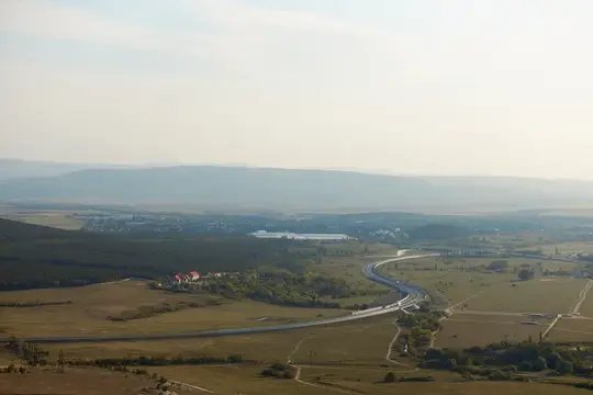 Вид с высоты птичьего полёта на живописную долину с дорогой и пролетающим над головой самолётом