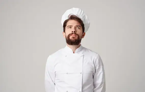 Задумчивый бородатый повар в белом колпаке и кителе