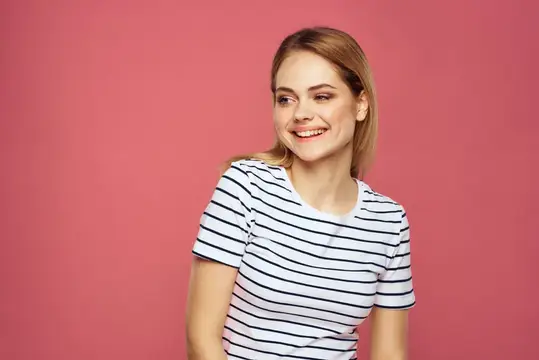 Улыбающаяся светловолосая девушка в полосатой футболке на розовом фоне