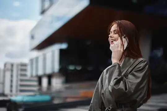 Рыжеволосая девушка весело говорит по телефону на городской улице