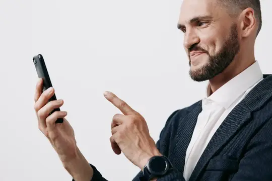 Улыбающийся бородатый мужчина в пиджаке смотрит в смартфон