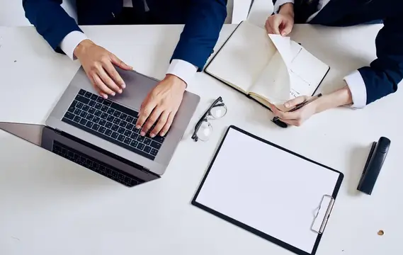 Руки деловых людей за работой с ноутбуком и блокнотом