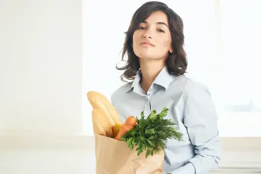 Молодая женщина с бумажным пакетом продуктов у окна