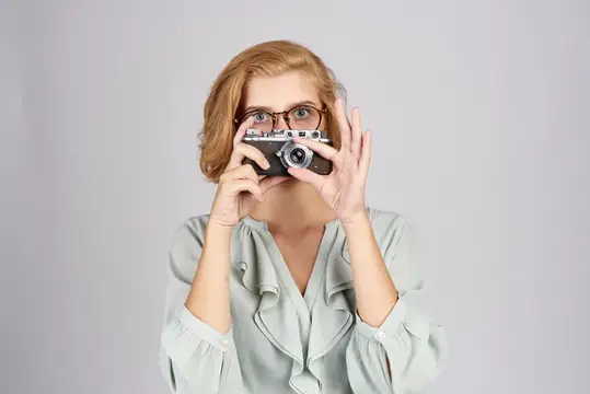 Рыжеволосая женщина в очках фотографирует на ретро-камеру
