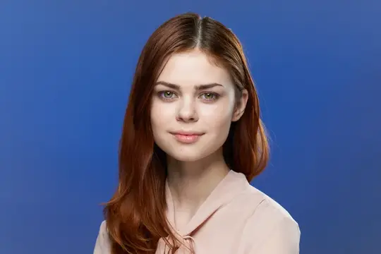 Рыжеволосая девушка смотрит в камеру на синем фоне
