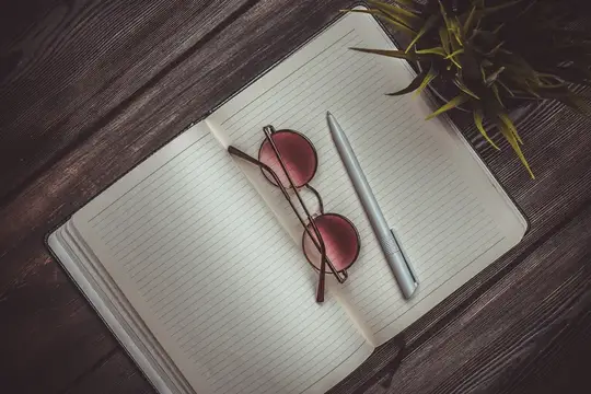 Блокнот, очки и цветок в горшке на деревянном столе, вид сверху, ручка, офис