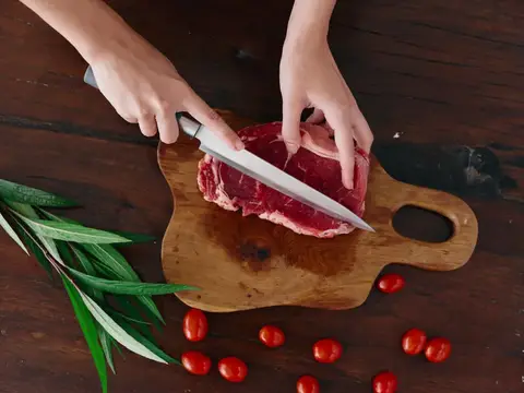 Женщина с ножом в руке нарезает свежее стейковое мясо для жарки на кухне