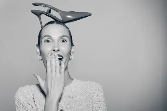 Удивлённая женщина с туфлей на голове прикрывает рот рукой