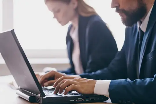 Мужчина и женщина в офисных костюмах работают за ноутбуками