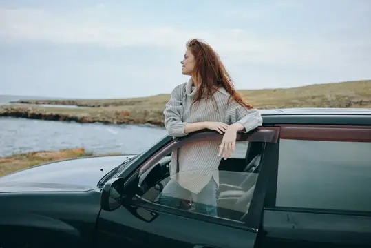 Рыжеволосая девушка у машины смотрит на море