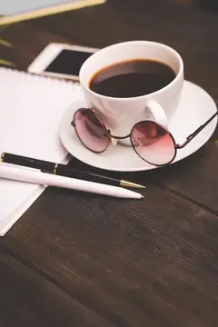 Чашка кофе на блюдце, деревянный стол, блокнот, ручка, офисные канцтовары