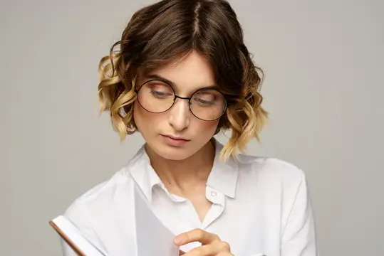 Молодая женщина в очках с книгой на сером фоне