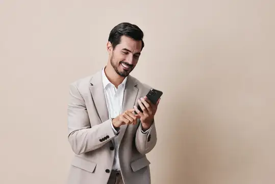 Улыбающийся мужчина в бежевом пиджаке смотрит в смартфон