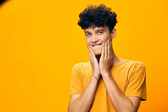 Улыбающийся кудрявый парень в жёлтой футболке на оранжевом фоне