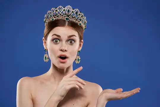 Удивлённая девушка в роскошной короне с изумрудами на синем фоне