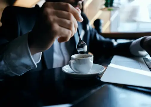 Мужчина в костюме размешивает кофе ложкой за столом с ноутбуком