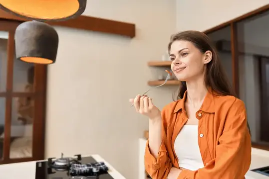 Молодая женщина в оранжевой рубашке пробует еду на кухне