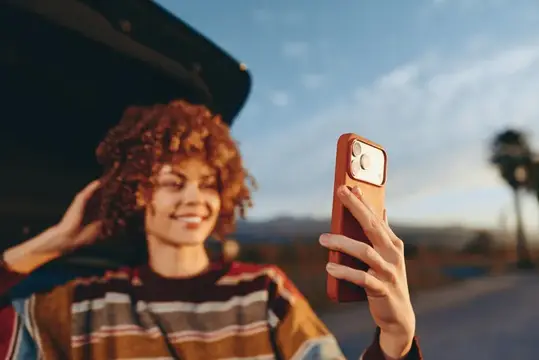 Рыжеволосая девушка делает селфи на смартфон на закате