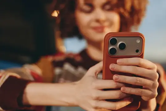 Улыбающаяся рыжеволосая девушка держит смартфон в красном чехле