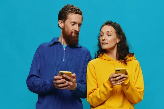 Бородатый мужчина и женщина в худи смотрят в смартфоны на синем фоне