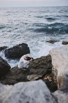 Девушка в белом платье сидит на камнях у бурного моря