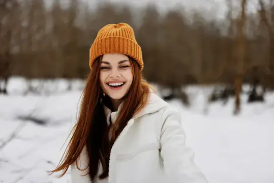 Улыбающаяся девушка в оранжевой шапке на зимней прогулке