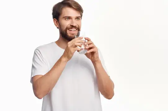 Улыбающийся бородатый мужчина пьёт воду из стакана