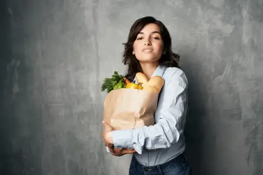 Молодая женщина с бумажным пакетом продуктов на сером фоне