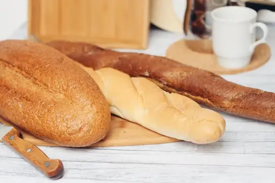 Свежий хлеб, багет и булочка на деревянной доске рядом с белой кружкой