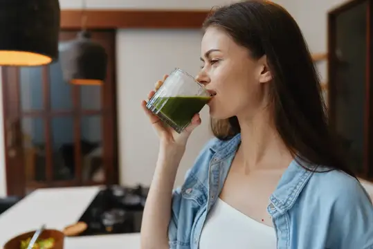 Молодая женщина пьёт зелёный смузи на светлой кухне
