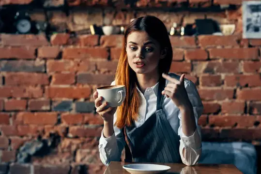 Молодая бариста с чашкой кофе указывает пальцем в кафе