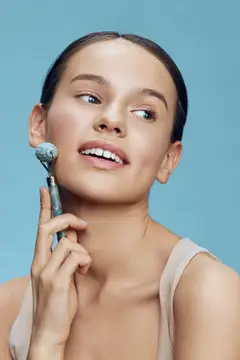 Молодая женщина с массажным роликом для лица на голубом фоне