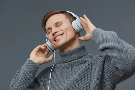 Молодой мужчина в наушниках слушает музыку с закрытыми глазами