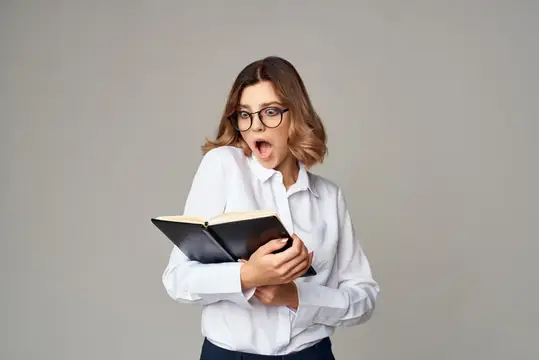 Удивлённая девушка в очках с раскрытой книгой