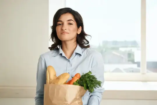 Молодая женщина с бумажным пакетом продуктов у окна