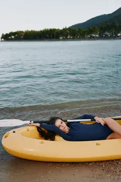 Девушка лежит в жёлтом каяке на берегу моря