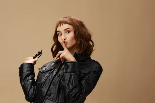 Молодая женщина в кожаной куртке прикладывает палец к губам
