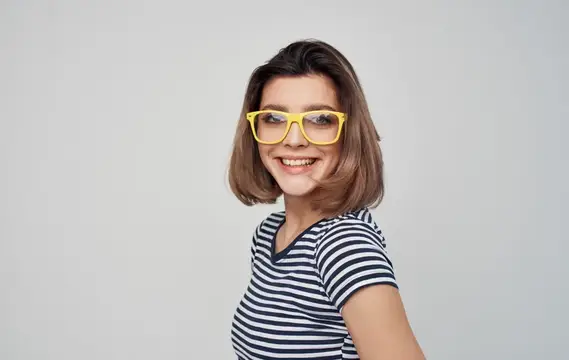 Улыбчивая девушка в жёлтых очках и полосатой футболке на сером фоне