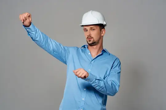 Мужчина в белой каске и голубой рубашке поднимает кулак вверх