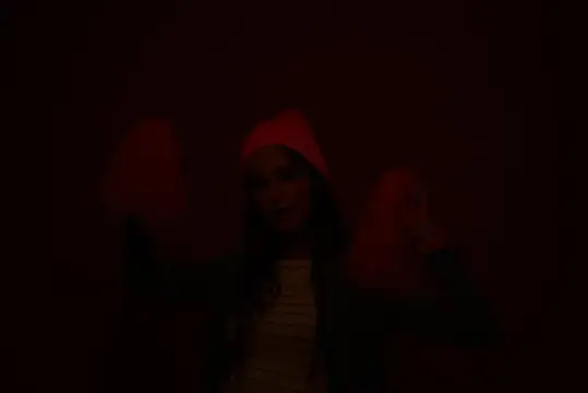Молодая женщина в красной шапке танцует в темноте